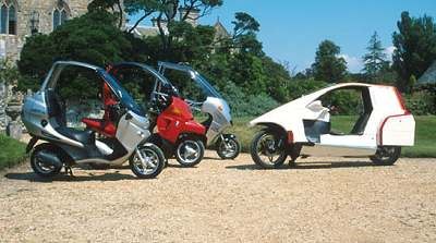 Due BMW C1 e un prototipo a tre ruote parcheggiati in un parco.