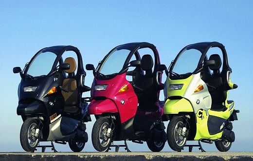 Tre BMW C1 nere, rosse e gialle affiancate su uno sfondo azzurro.