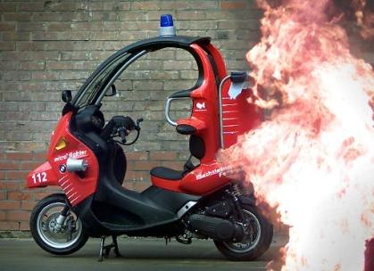 BMW C1 rossa con allestimento dei vigili del fuoco, fotografata accanto a una scenografia con fiamme.