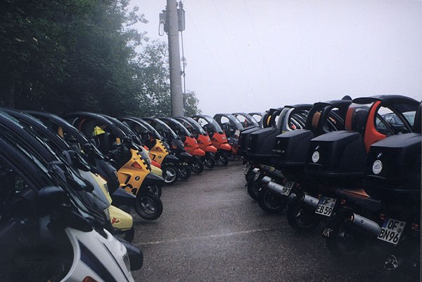 Numerose BMW C1 parcheggiate in due file lungo un vialetto.
