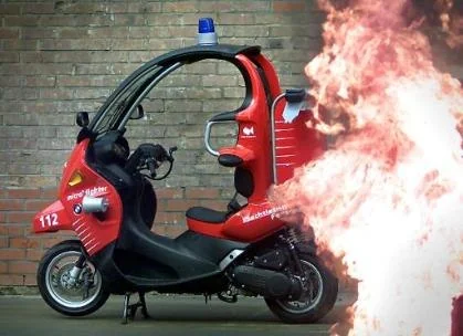 BMW C1 rouge aménagée pour les sapeurs-pompiers, photographiée devant un décor représentant des flammes.